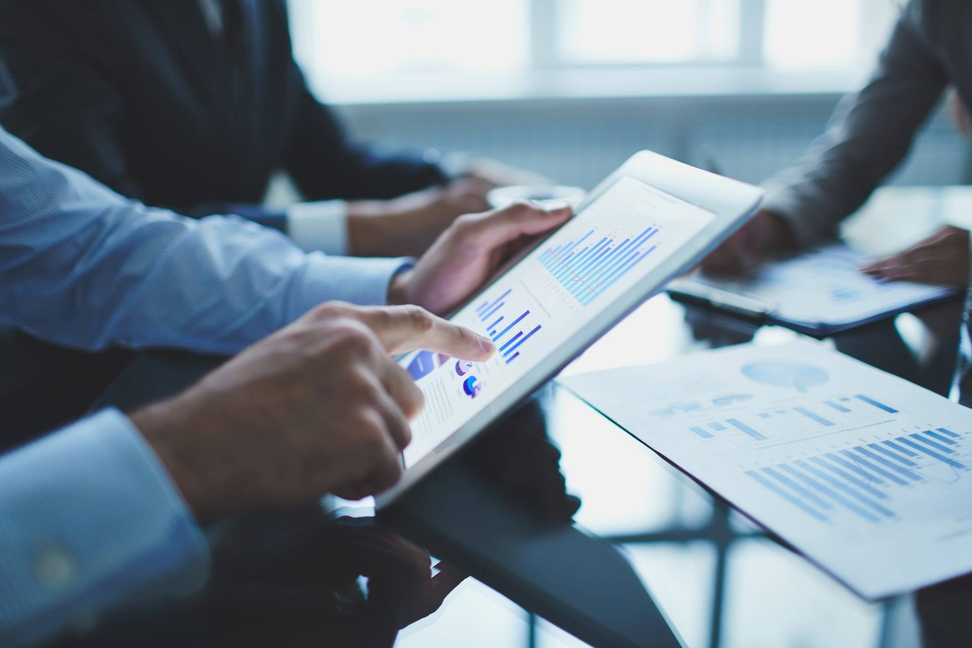 Profissionais analisam relatórios financeiros em um tablet durante uma reunião.