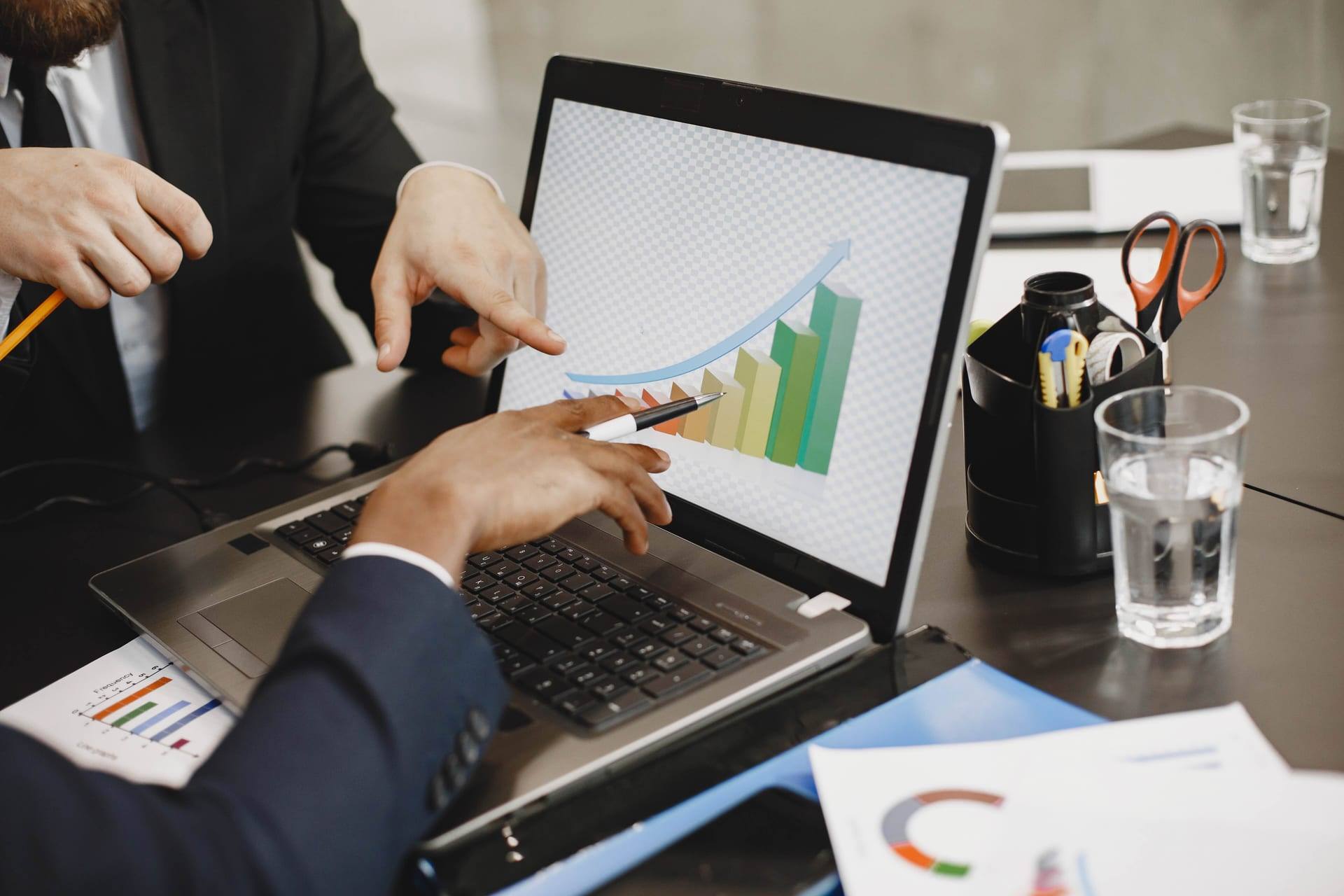 Dois executivos analisam um gráfico de crescimento na tela de um notebook.